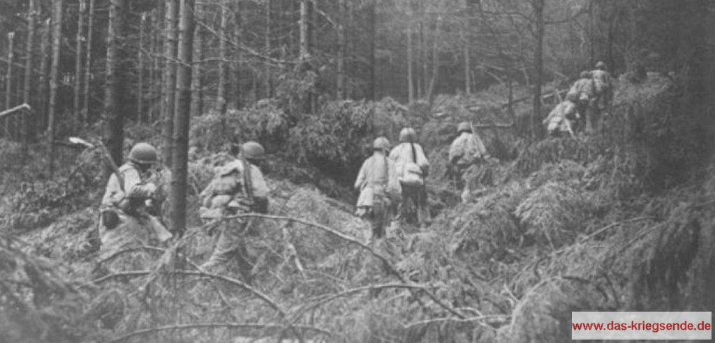 Auf dem Weg zur Front durchqueren Infanteristen der 8. US-ID einen durch Granatbeschuss beschädigten Wald westlich von Siegen.